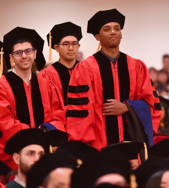 Three graduating medical students walk to the stage.