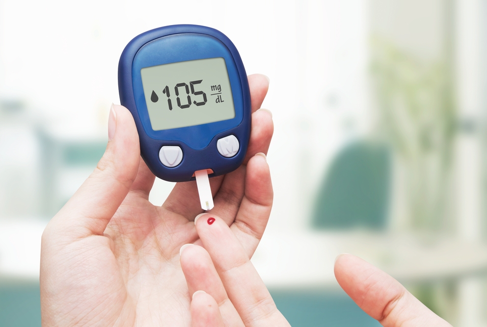 photo of hand holding a glucometer near a finger with drop of blood on it